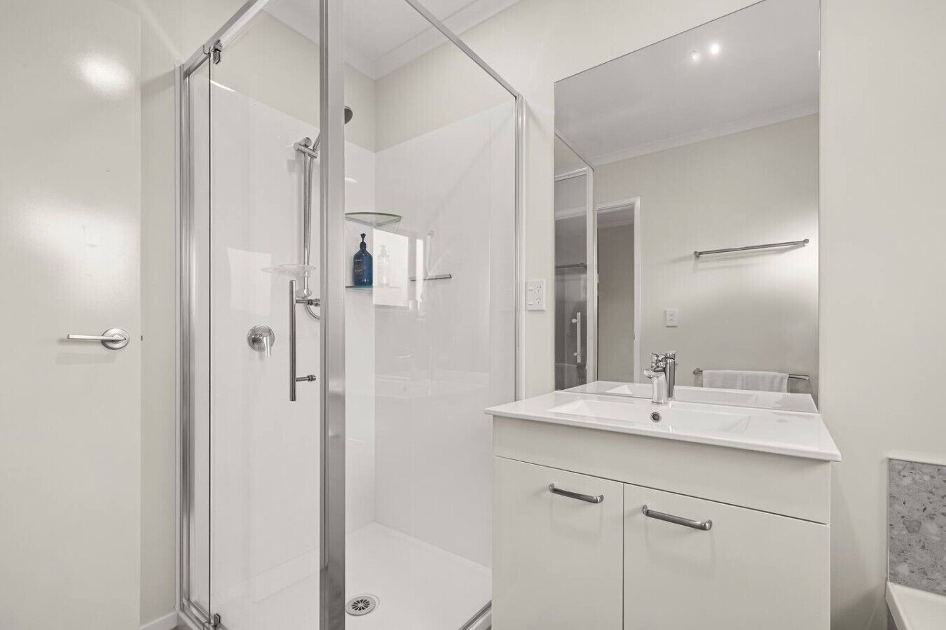 A modern bathroom with a glass shower enclosure, a white sink, and a large mirror.