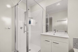 A modern bathroom with a glass shower enclosure, a white sink, and a large mirror. - Rotorua 3BR Adventure Base with Air-Con & Parking (Rotorua)