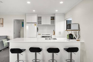 A modern kitchen with white cabinets, a built-in microwave, and a bar area with four stools. - Rotorua 3BR Adventure Base with Air-Con & Parking (Rotorua)