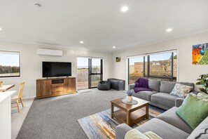 Una sala de estar moderna con un televisor de pantalla plana, un sofá gris, un mueble de madera y un puerta corrediza de vidrio que da a un patio.
