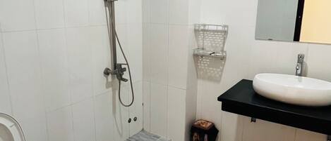 A bathroom with a toilet, a shower, a sink, and a mirror.