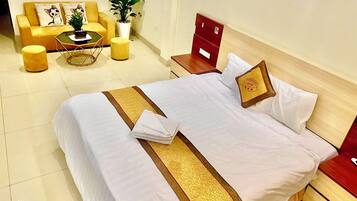 A neatly made bed with a white and gold bedspread, a small bedside table with a lamp, and a red nightstand with a wooden drawer.