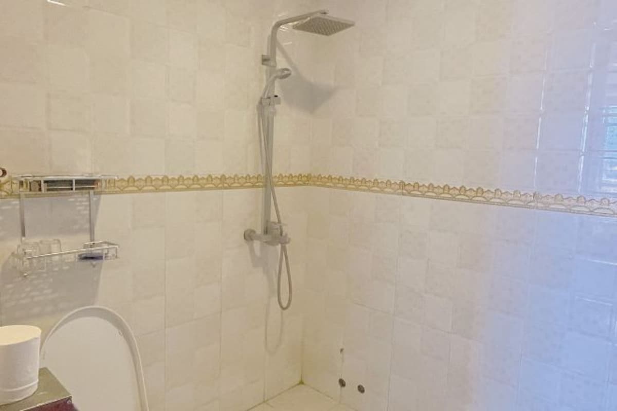 A shower with a handheld showerhead, a glass shower caddy, and a white chair.
