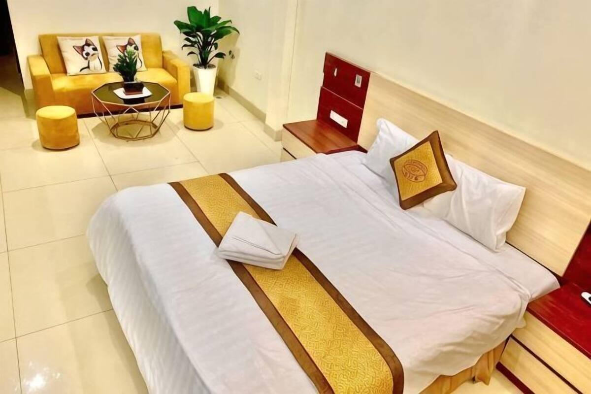 A neatly made bed with a white and gold bedspread, a red headboard, and a small bedside table with a lamp.