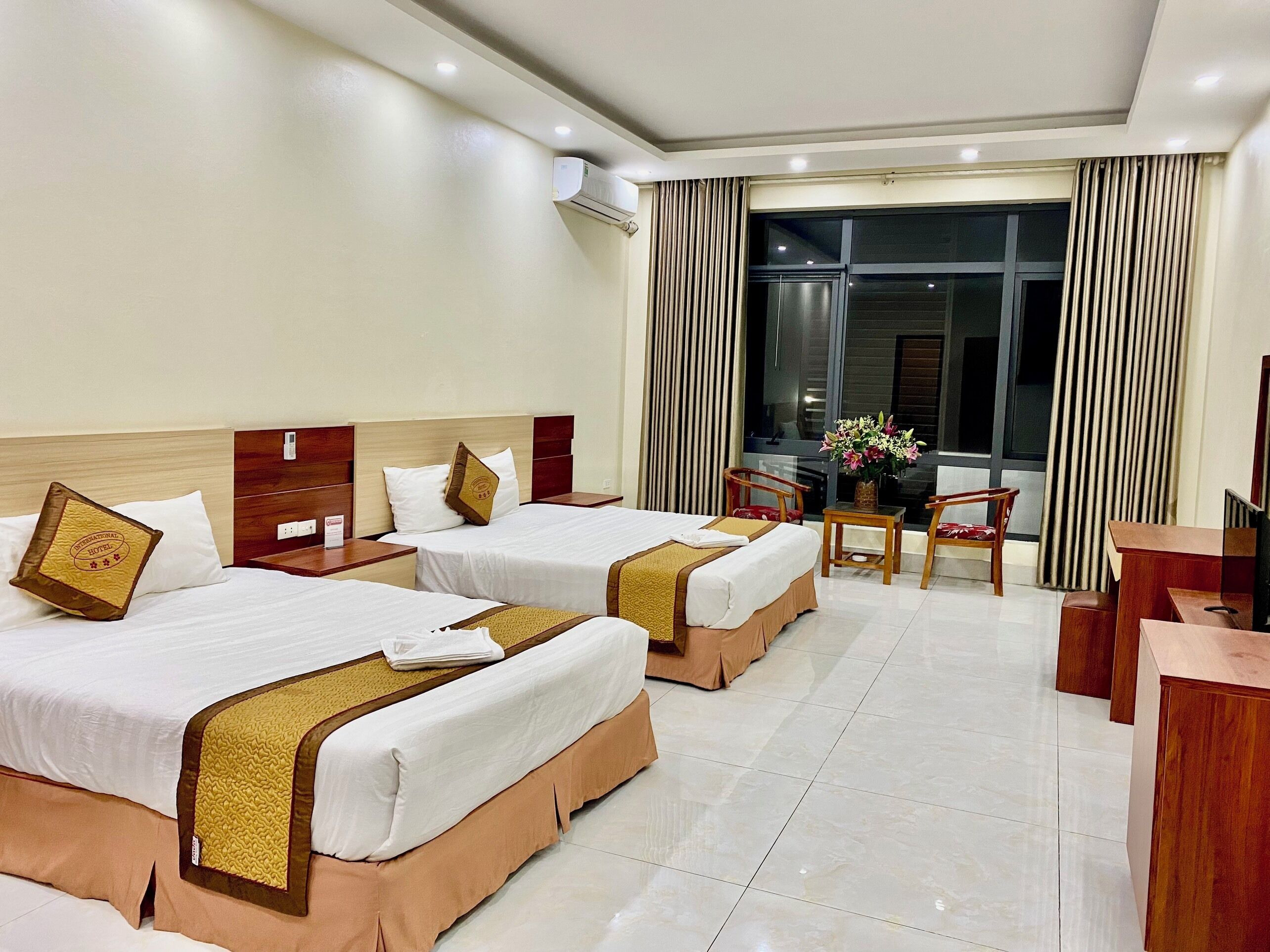 Habitación de hotel con dos camas, un escritorio, una silla y un ventanal con cortinas.