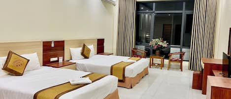 Habitación de hotel con dos camas, un escritorio, una silla y un ventanal con cortinas.
