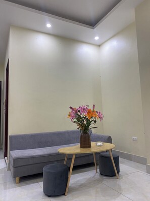 A modern living room with a grey sofa, a round wooden table, and a vase of flowers. - Dong Thanh Hotel (Bac Ninh)