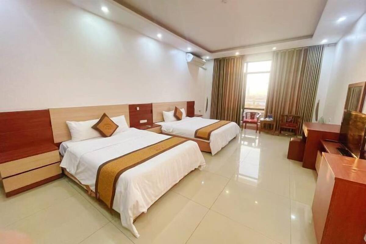 A hotel room with two beds, a desk, a chair, and a television.