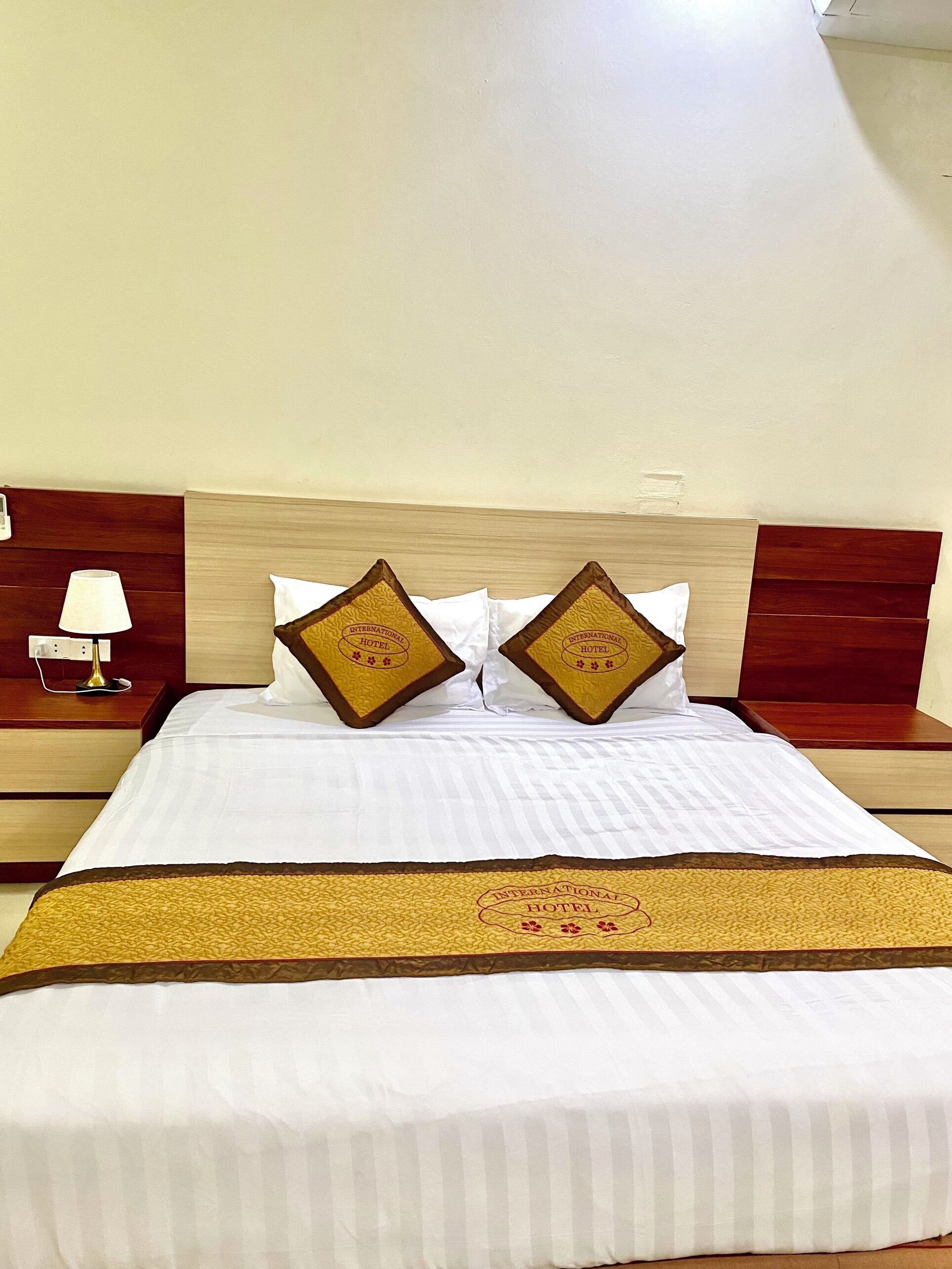 Habitación de hotel con cama, dos almohadas con un logotipo, una lámpara de noche y una mesita de noche.