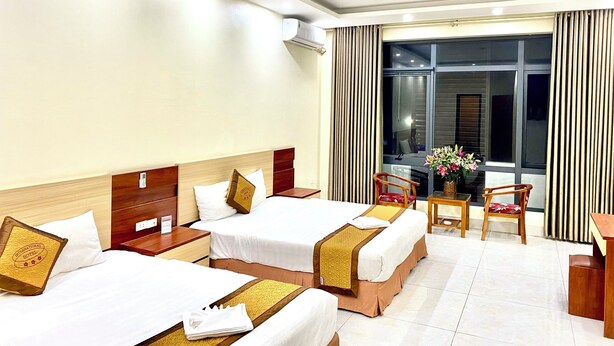 A hotel room with two beds, a desk, a chair, and a large window. - Dong Thanh Hotel (Vo Cuong)