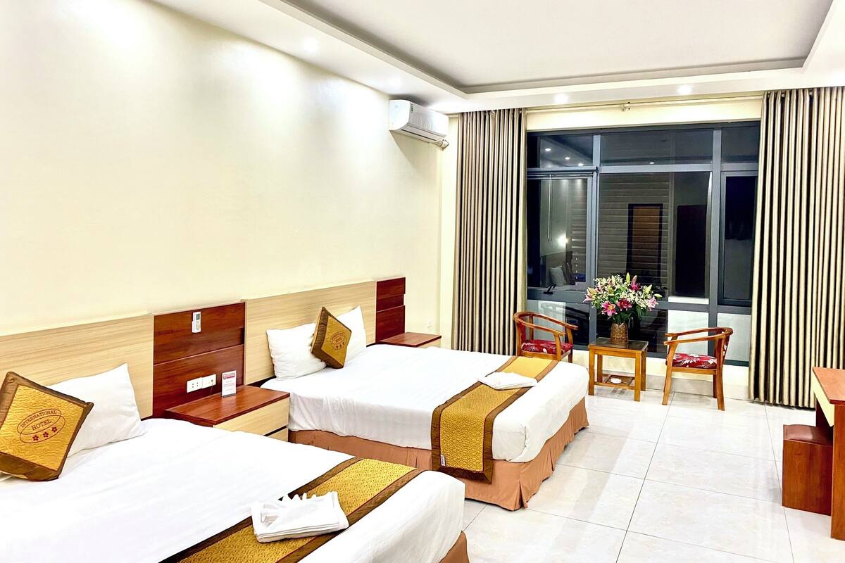 A hotel room with two beds, a desk, a chair, and a large window.