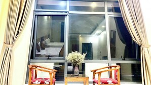A room with a large window, two wooden chairs, a small table, and a vase with flowers. - Dong Thanh Hotel (Vo Cuong)