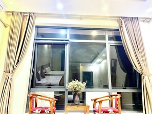 A room with a large window, two wooden chairs, a small table, and a vase with flowers. - Dong Thanh Hotel (Bac Ninh)