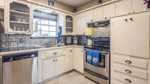 Una cocina con armarios blancos, lavavajillas de acero inoxidable, horno negro y ventana con vistas.
