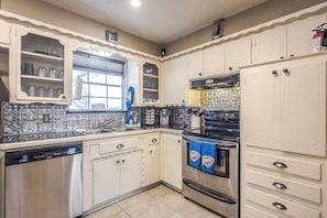 A kitchen with white cabinets, a stainless steel dishwasher, a black oven, and a window with a view.