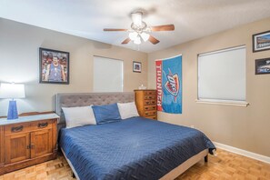 A bedroom with a bed, a nightstand, a dresser, a ceiling fan, and a wall with a sports banner.