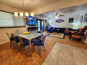 Ein Wohnzimmer mit Fernseher, Sitzgelegenheiten und Deckenventilator.