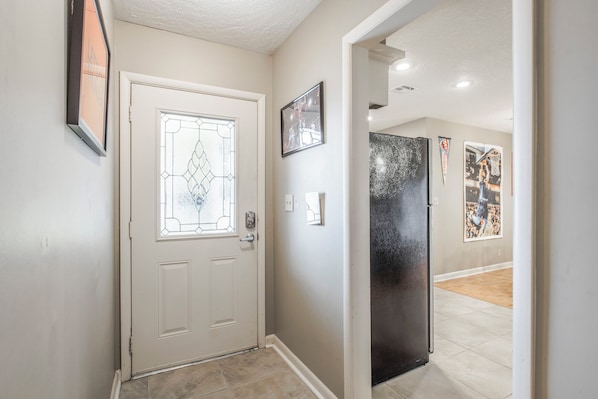A hallway with a white door, a refrigerator, and wall-mounted pictures.