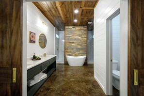 Un bany modern amb una banyera autònoma, un lavabo amb mirall i una paret d'accent de pedra.