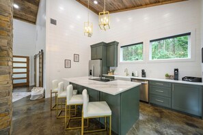 A modern kitchen with a central island, green cabinets, and a large window. - Secluded, Hot Tub, Games, Luxury, Fire pit, Pets (Broken Bow)
