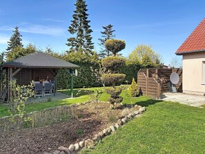 Un jardin avec un patio couvert, un abri en bois et une pelouse bien entretenue.