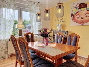Un coin repas avec une table en bois, des chaises, des luminaires suspendus et un vase décoré de motifs floraux.