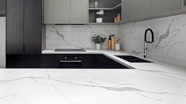 Een moderne keuken met marmeren aanrechtbladen, een zwarte kraan en grijze kastjes.