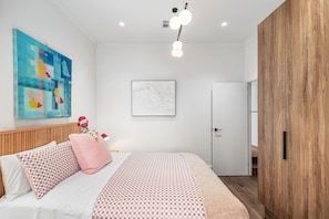 A bedroom with a bed, pillows, a wall art piece, a framed picture, a wooden wardrobe, and a ceiling light fixture. - COLLINGWOOD HAVEN-3beds, 4 bath +GARAGE -6 guests-Walk to CBD, stylish open plan (Collingwood)