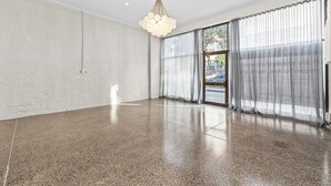 Een ruime kamer met een gepolijste betonnen vloer, grote ramen voorzien van transparante gordijnen en een moderne kroonluchter.