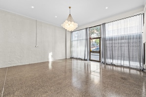 Ein geräumiges Zimmer mit einem polierten Betonboden, großen Fenstern mit durchsichtigen Vorhängen und einem modernen Kronleuchter.