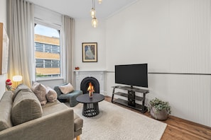 Ein modernes Wohnzimmer mit Kamin, einer Sofagarnitur, einem Fernseher und einem Blumentopf.