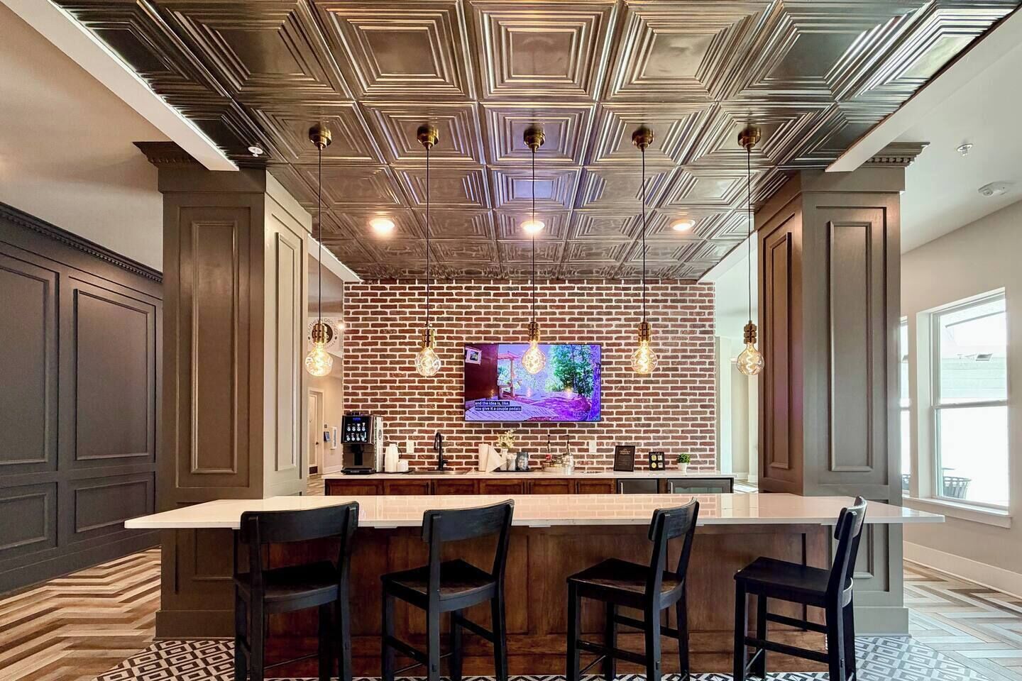 Un espace bar avec un mur en briques, un grand écran de télévision et des luminaires suspendus.