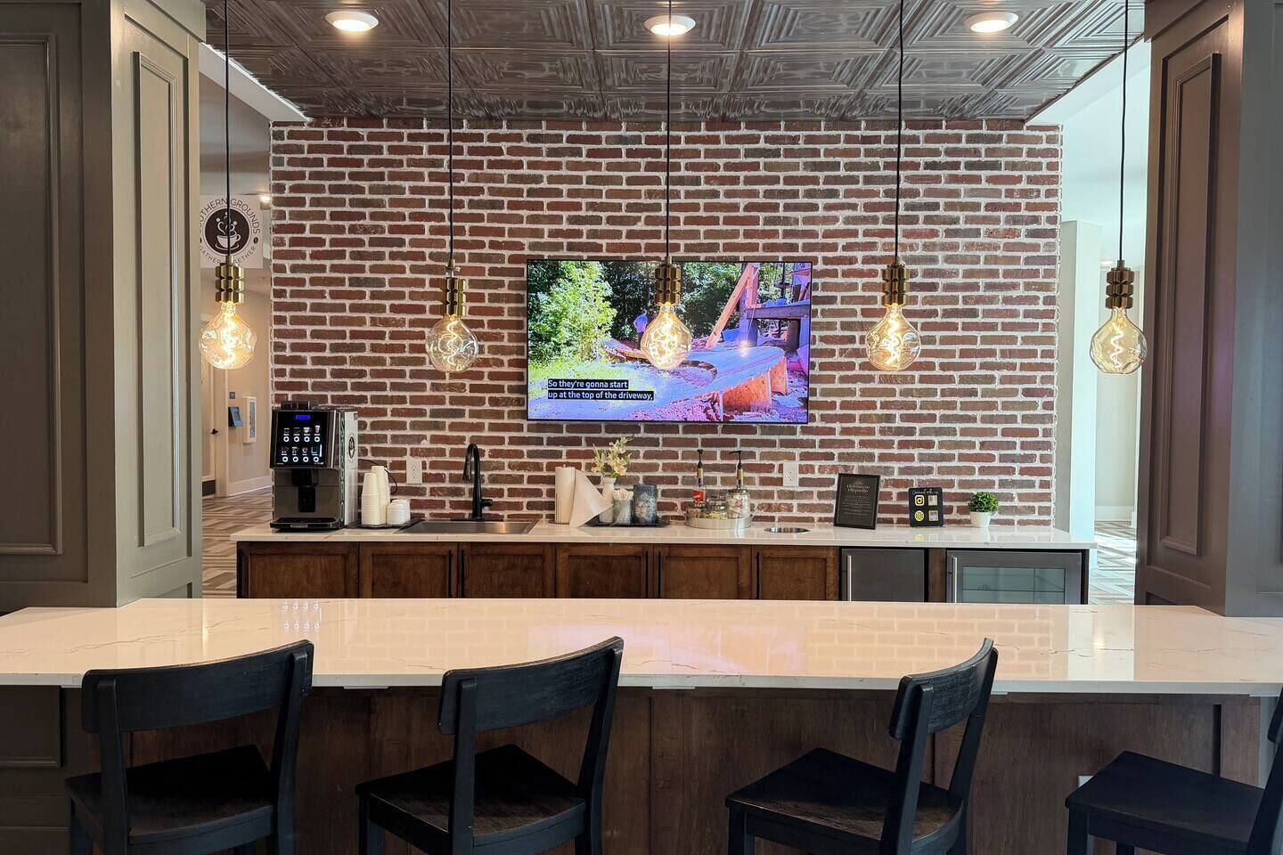 Une cuisine moderne avec un mur en briques, un grand téléviseur, des luminaires suspendus et un coin bar avec des chaises.