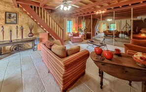 Ein geräumiges Wohnzimmer mit Treppe, einem Sofa, einem Tisch mit roten Vasen und einem Spiegel, der den Raum reflektiert.