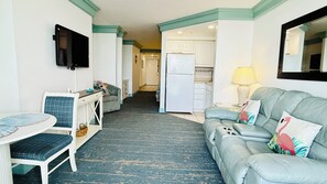 Ein Hotelzimmer mit Esstisch, einer Sitzecke, einem an der Wand befestigten Fernseher, einer Küchenzeile und einem Spiegel.