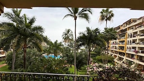 A balcony with a table and chairs, overlooking a landscaped area with palm trees and a building with balconies. - Velas Vallarta Beach Front Resort (Puerto Vallarta)