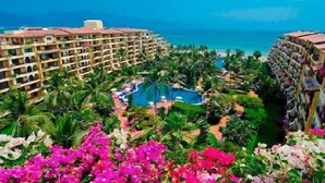 A resort with a pool, palm trees, and a view of the ocean. - Velas Vallarta Beach Front Resort (Puerto Vallarta)