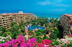 A resort with a pool, palm trees, and a view of the ocean. - Velas Vallarta Beach Front Resort (Puerto Vallarta)