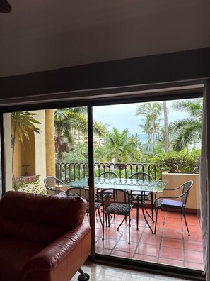 A balcony with a glass table and chairs, a leather sofa, and a view of palm trees and buildings. - Velas Vallarta Beach Front Resort (Puerto Vallarta)