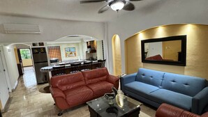 A living room with a ceiling fan, a blue sofa, red leather chairs, and a kitchen in the background. - Velas Vallarta Beach Front Resort (Puerto Vallarta)