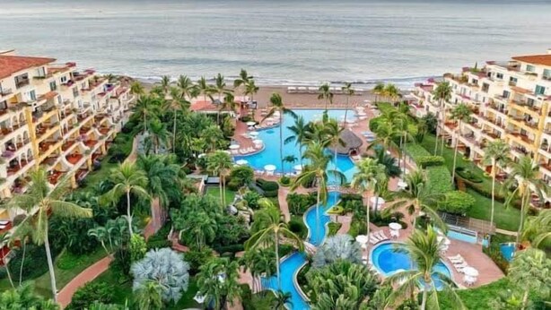 A resort with multiple swimming pools, palm trees, and a view of the ocean. - Velas Vallarta Beach Front Resort (Puerto Vallarta)