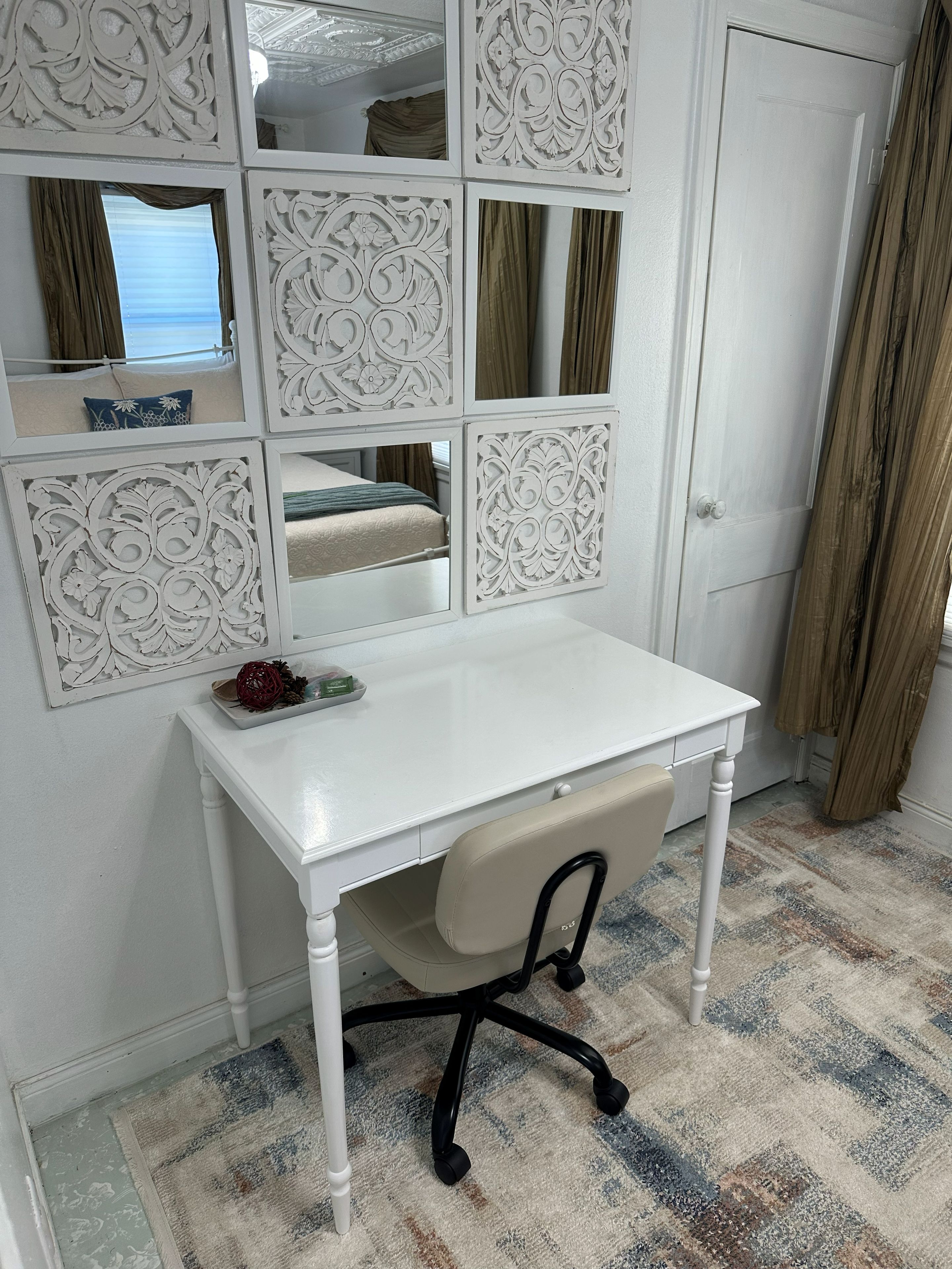 A white desk with a chair in a room with patterned walls and a door.