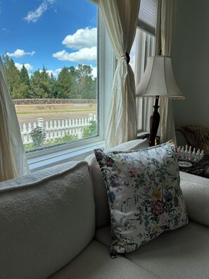 Una habitación con sofá, lámpara y vistas a una cerca blanca y árboles.