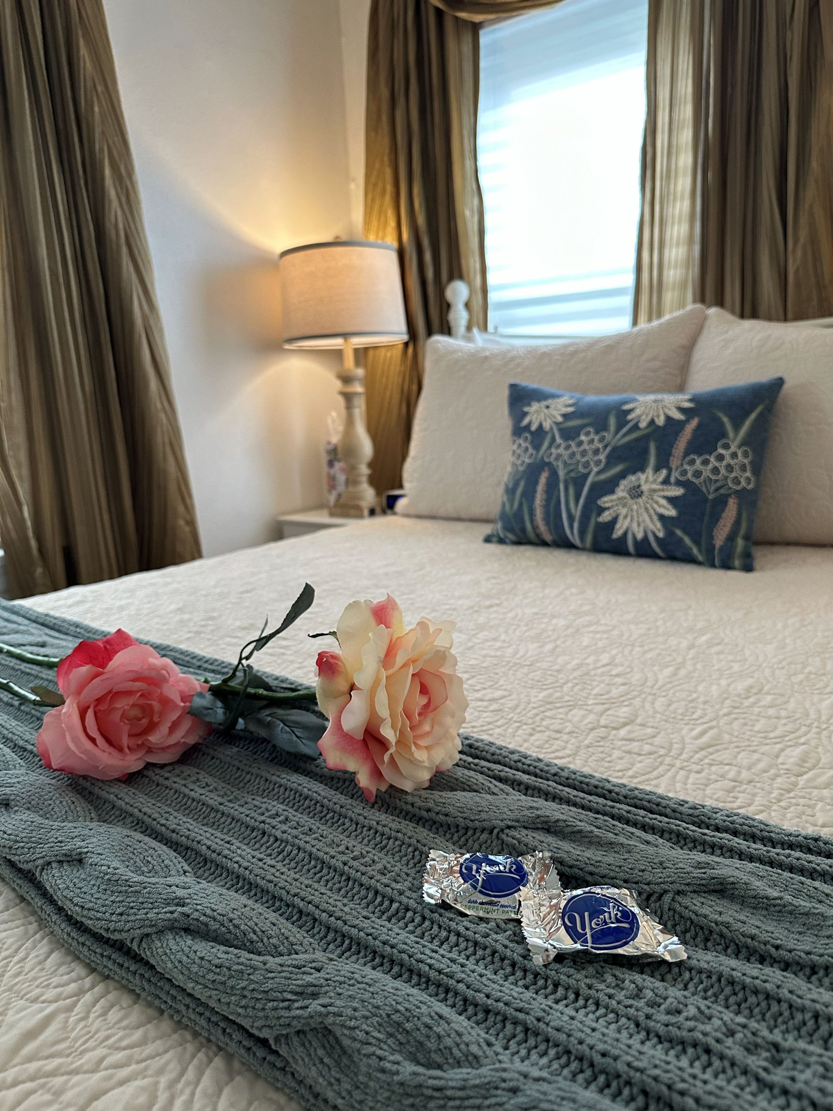 Una cama con un edredón tejido, dos almohadas y un ramo de rosas.