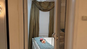 A bedroom with a bed, a chandelier, a window with curtains, and a radiator. - Granny’s Corner Suite - 2 bed home near Medora, Theodore Roosevelt National Park (Dickinson)