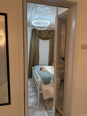 Une chambre Ă coucher avec un lit, un lustre, une fenĂȘtre avec des rideaux et un radiateur.