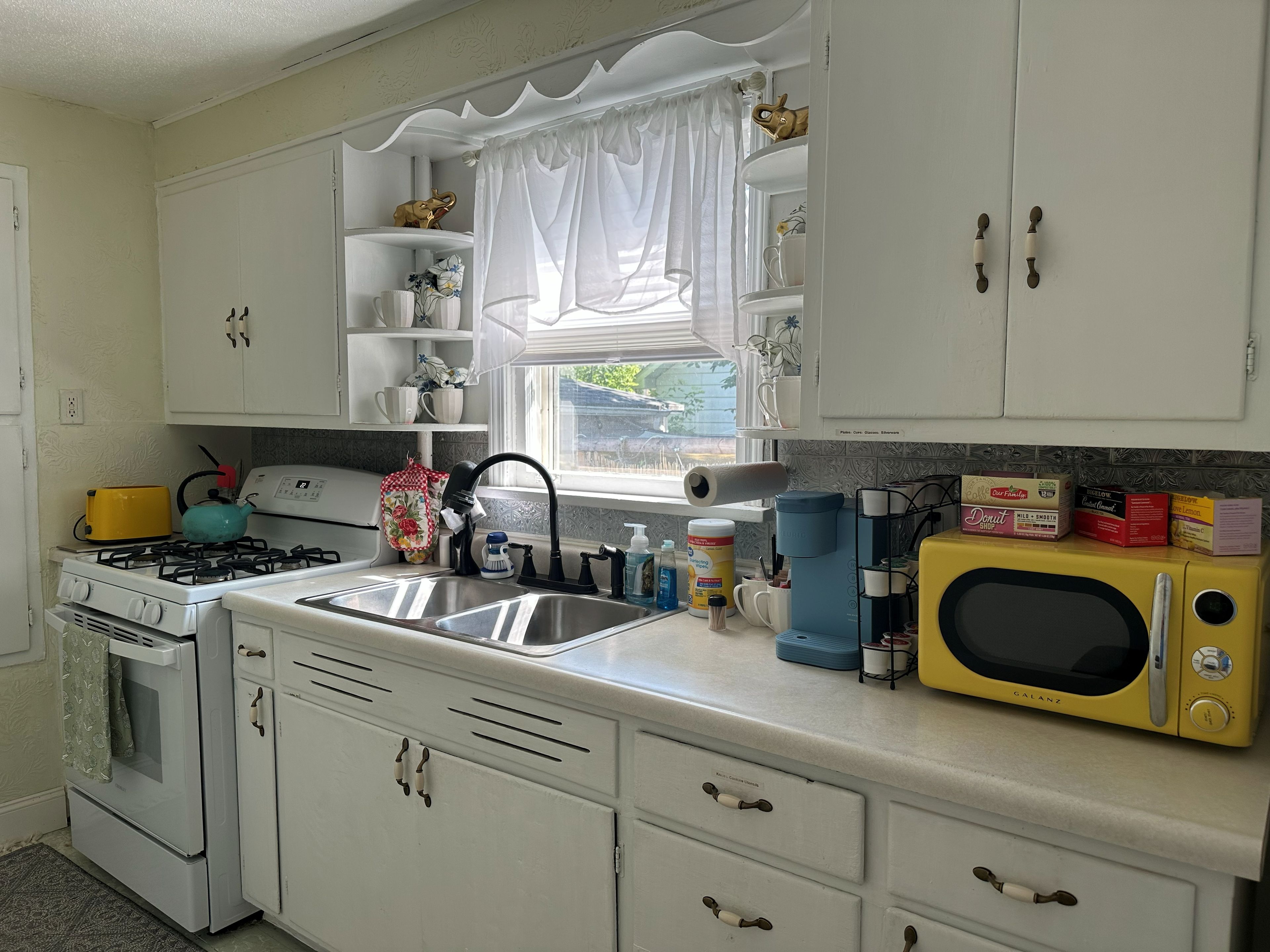 A kitchen with white cabinets, a yellow microwave, a stove, and a window with a curtain.
