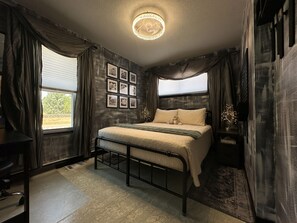 Un dormitorio con cama, escritorio y ventana con cortinas.