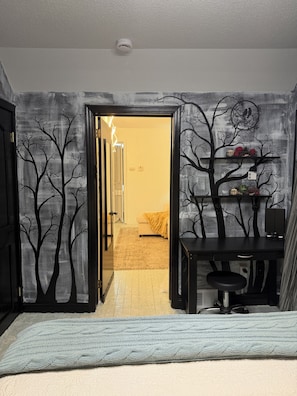 Una habitación con cama, escritorio y silla. Hay una puerta que da a otra estancia.