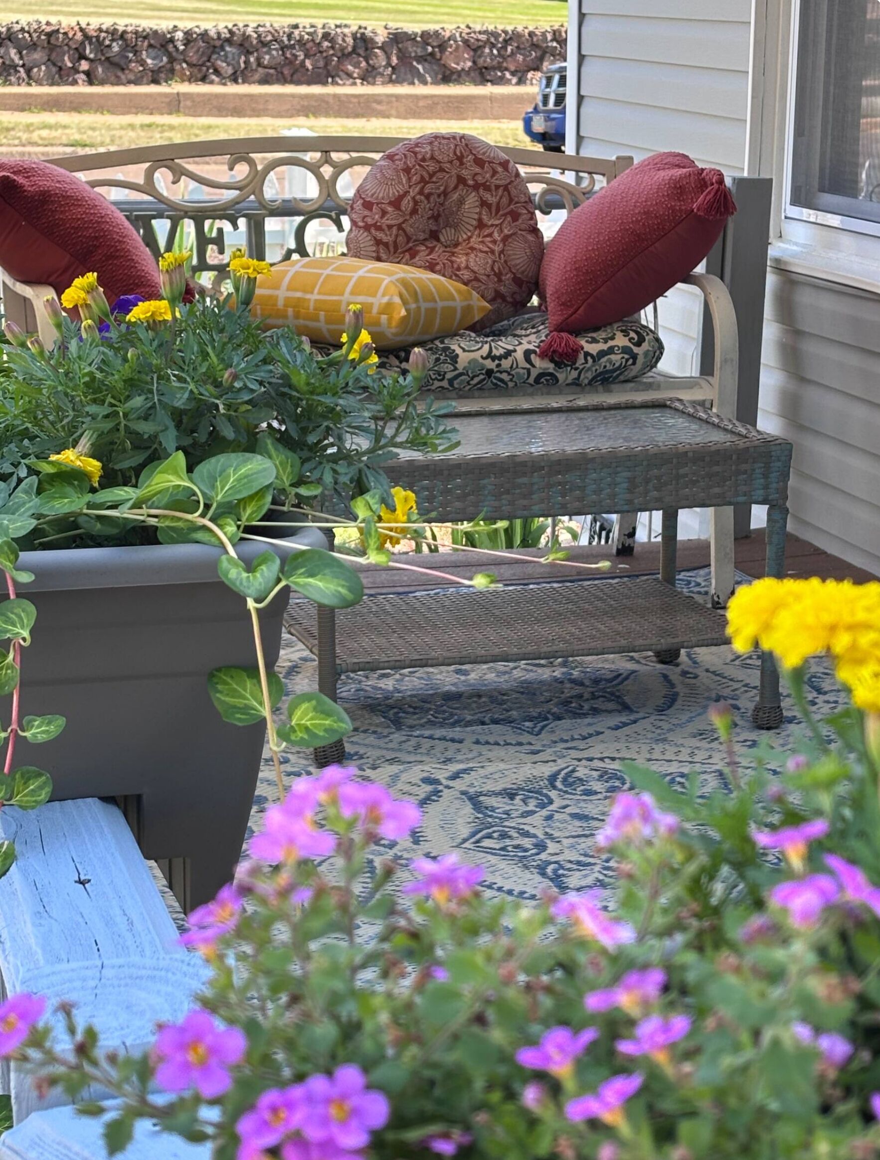 A porch with a chair, a bench, and a potted plant with flowers.